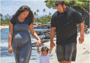 A native Hawaiian pregnant woman holding hands and walking with a small child and native Hawaiian man.