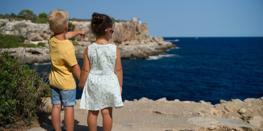 A young boy and girl holding hands look out over the ocean.