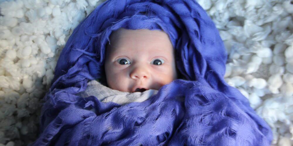 This newborn, surrounded by a purple scarf is wide-eyed and eager to see what is around her.