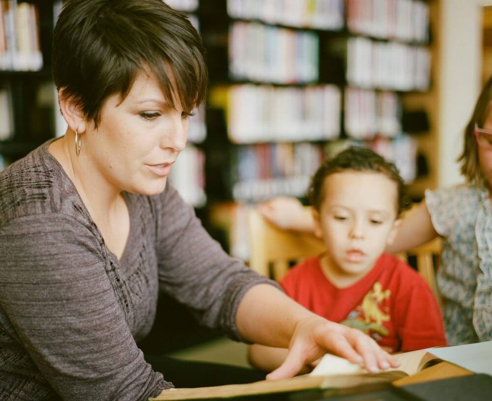 Mother reading to children inside of a library. Books in the background holding a book, kids looking and listening intently.https://www.instagram.com/AwCreativeUT/
https://www.awedcreative.com/
https://www.awcreativeut.com
#AwCreativeUT #awcreative #AdamWinger Adam Robert Winger