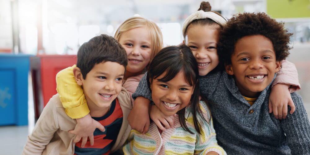 Portrait, group and kids with smile at school for education, learning and knowledge with hug. Student, children or face with happiness in classroom for study, scholarship or childhood development Five kids smiling and hugging
