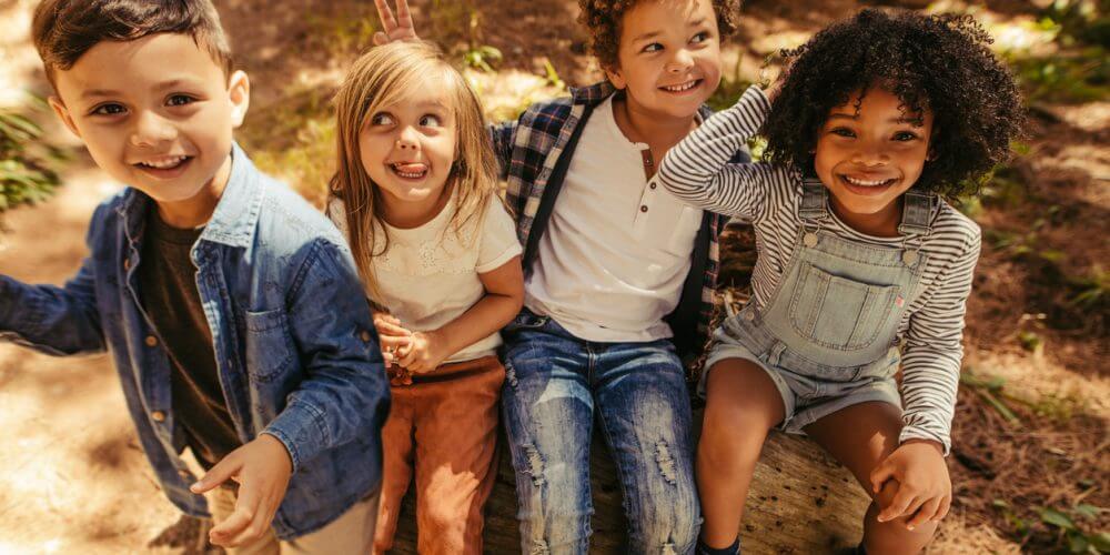 Multi-ethnic group of kids sitting on a log and laughing.