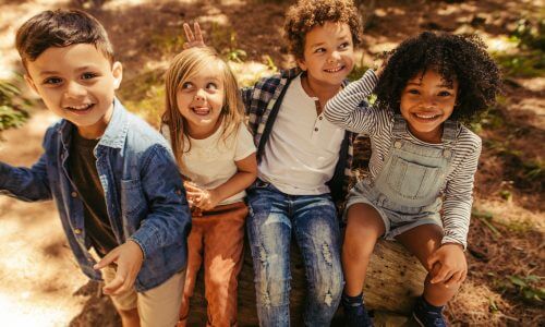 Multi-ethnic group of kids sitting on a log and laughing.