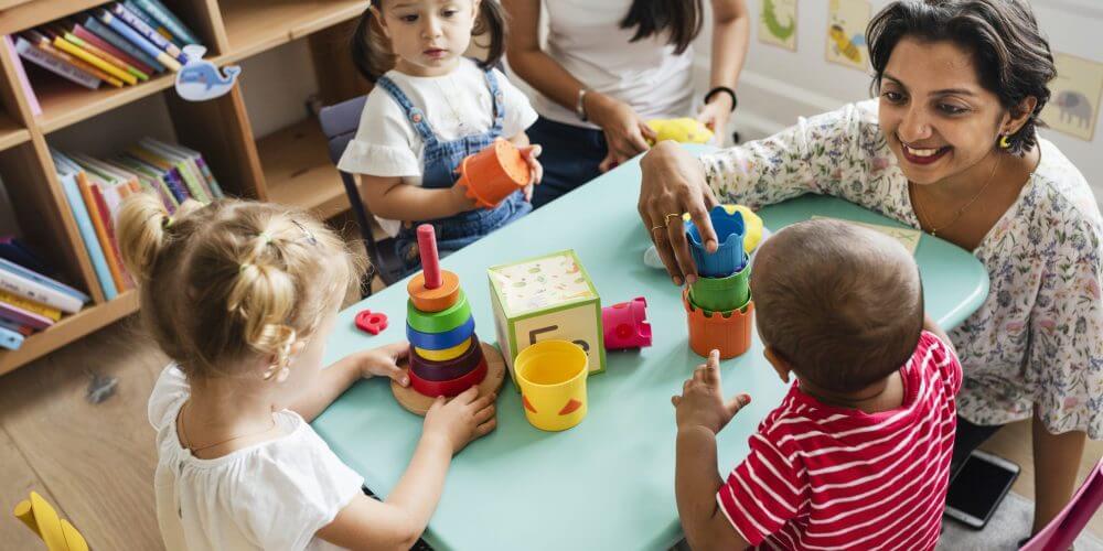 Early education teacher sitting at a table with children playing