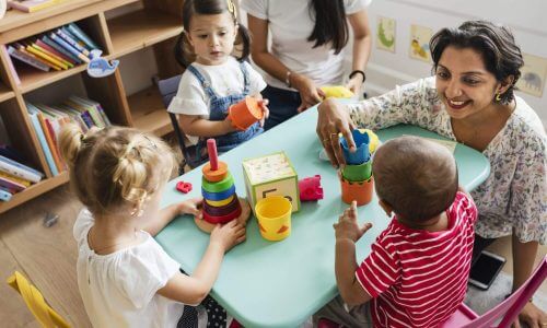Early education teacher sitting at a table with children playing